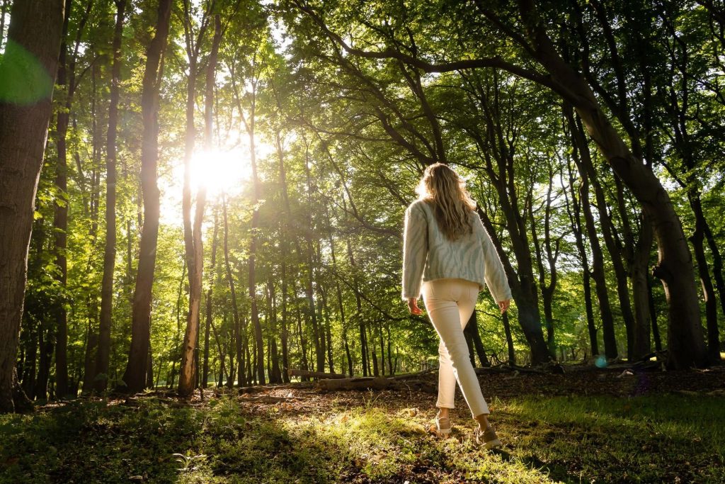 Frau geht durch die Natur und richtet ihre Aufmerksamkeit bewusst auf sich und ihren Körper.