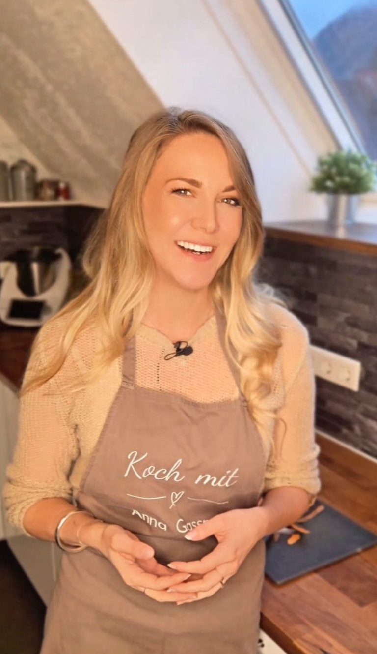 Anna Gassner von Klar gesund trägt eine Schürze in einer modernen Küche und lächelt.