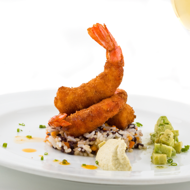 Frittierte Garnelen auf einem Bett aus Reis mit Avocado und Sauce serviert.