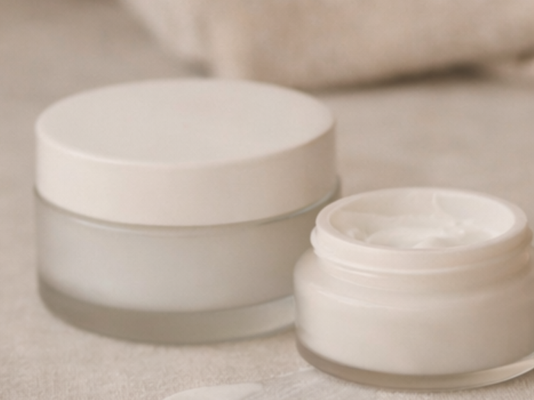 Zwei Cremebehälter, einer groß und einer klein, auf einer neutralen Oberfläche.