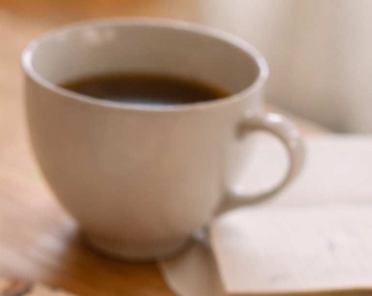 Tasse mit Tee auf einem Holztisch, daneben ein Stück Papier.