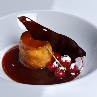 Ein cremiger Pudding mit Sauce, garniert mit Kirschen und einer feinen Krokantscheibe.