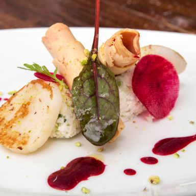 Gourmet-Gericht mit Jakobsmuscheln, Gemüse, einer Beilage und roter Sauce dekorativ angerichtet.